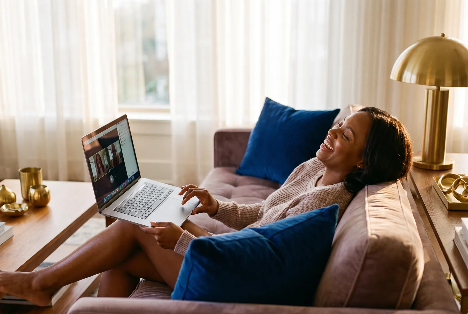Une femme détendue sur son canapé, riant pendant une téléconsultation vidéo sur son ordinateur portable